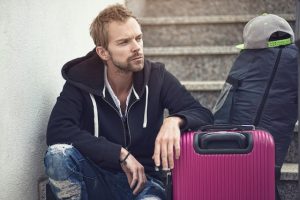 Man sitting next to a suitcase and a packed bag